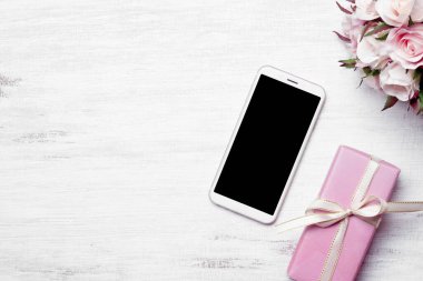 Mockup beyaz akıllı telefon, boş siyah ekranlı ev grunge ahşap arka planda Noel ve yeni yıl için hediye kutusu, Velentine 'in günü, düğün hediyesi konsepti, fotokopi alanı olan Mockup cep telefonu..