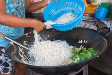 Kadın fasulye filizi ile tavada kızartılmış erişte yemek yapıyor.