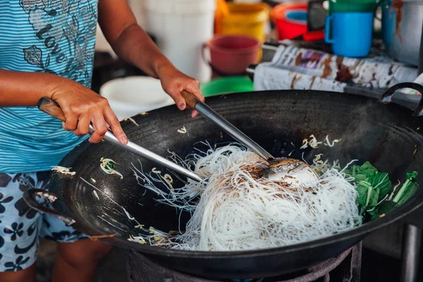 Kadın fasulye filizi ile tavada kızartılmış erişte yemek yapıyor.