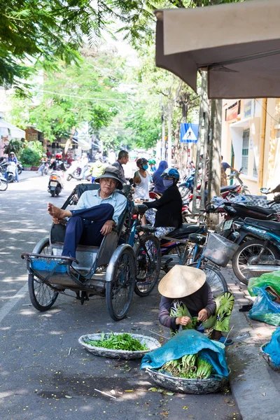 Mujer vietnamita en sombrero cónico tradicional está clasificando verdes sentados en el suelo — Foto de Stock