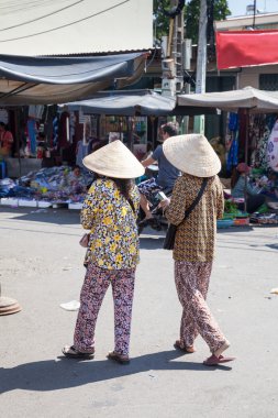 Vietnamese women in traditional conical hat sell lottery tickets on the streets of Nha Trang clipart