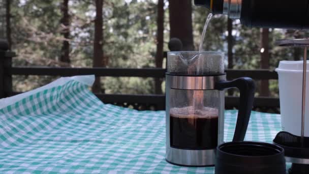 커피를 끓이고, 숲 속의 피크닉 테이블에 있는 렌치 프레스에 커피를 붓는다 — 비디오
