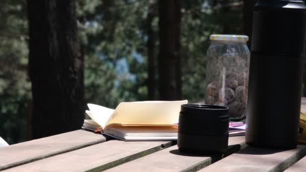 Notebook pagina, De wind verplaatst de pagina van een notebook op de picknicktafel — Stockvideo