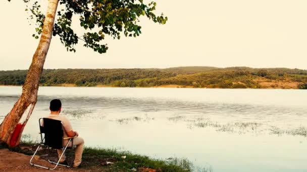 Hombre observando el lago, hombre observando la vista del lago en otoño cerca del árbol — Vídeos de Stock