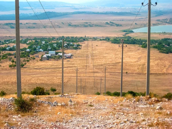Bozkırdaki tepelerin arasındaki elektrik hattı. Manzara, tepeler, dağlar, bozkır, rüzgar, ot, portakal, kuraklık. Bozkırdaki yeşil çalılar. Elektrik hattı tepeden aşağı simetrik olarak kurumuş bozkırların arasında akıyor..