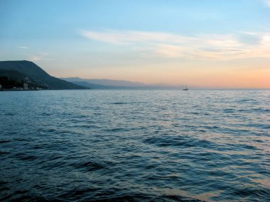 Yaz mevsiminde deniz kıyısında. Dağlar, yat. Sahil şeridine bakan deniz manzarası. Kıyı şeridi. Deniz. Sakin denizdeki kayalar. Güneş doğarken deniz.