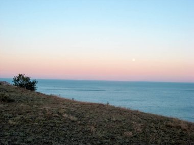 Deniz manzaralı dağ manzarası. Denize bakan bir tepedeki vahşi çalı. Dağlarda deniz tarafından gün batımı. Hiç kimse, manzara, dağlar, deniz, sessizlik.
