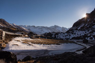 And Dağları 'nda karlı bir dağ manzarası, ufukta güneş ve kullanılmayan eski bir tren hattı. Las Cuevas, Mendoza, Arjantin