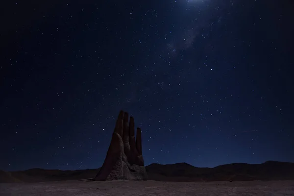 Hand of the desert in Antofagasta, Chile. Night long exposure shot with sky full of stars. Moonlight and a shooting star can be seen.