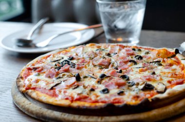 Kapalı, ahşap tepside servis edilen, ahşap tabakta servis edilen, çatal ve kaşıkla servis edilen, ahşap masa üzerinde bir bardak su ve koyu tonda servis edilen, beyaz tabağın arka planında.