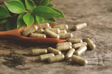 Kapalı, ahşap kaşıkta bitkisel kapsül ve koyu kahverengi tonda grunge arkaplan.