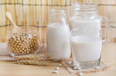 Kapanmış taze organik soya sütü cam şişede taze tohumlar ahşap arka planda yumuşak ışık tonunda