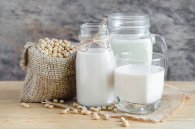 Kapanmış taze organik soya sütü cam şişede ve tahta zemin üzerinde taze tohumlar var.