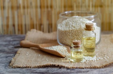 Closed up sesame oil in glass bottle with dry seeds in bowl and wooden spoon on grunge background in soft yellow tone