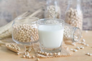 Closed up soybean milk in glass over blur soybean seed and milk in glass bottle and jug background, for healthy food and agricultural product concept
