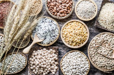 Çeşitli türde kuru organik tahıl ve tahıl tohumları tahtadan ve seramik kaseler koyu tonda, sağlıklı veya temiz gıda malzemeleri veya tarım ürünleri konsepti için.