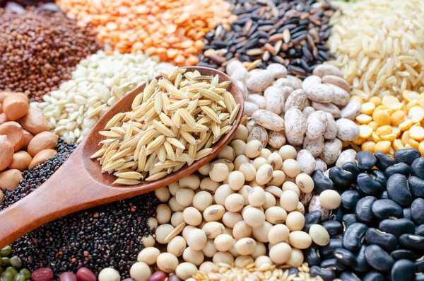 Dry rice seeds in wooden spoon on variety kinds of natural cereal and grain seed background,, for food industry or agricultural product concept