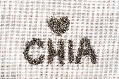 Kuru organik chia tohumu CHIA sözcüğünde. Beyaz çuval kumaş arka planında küçük kalp şeklinde.