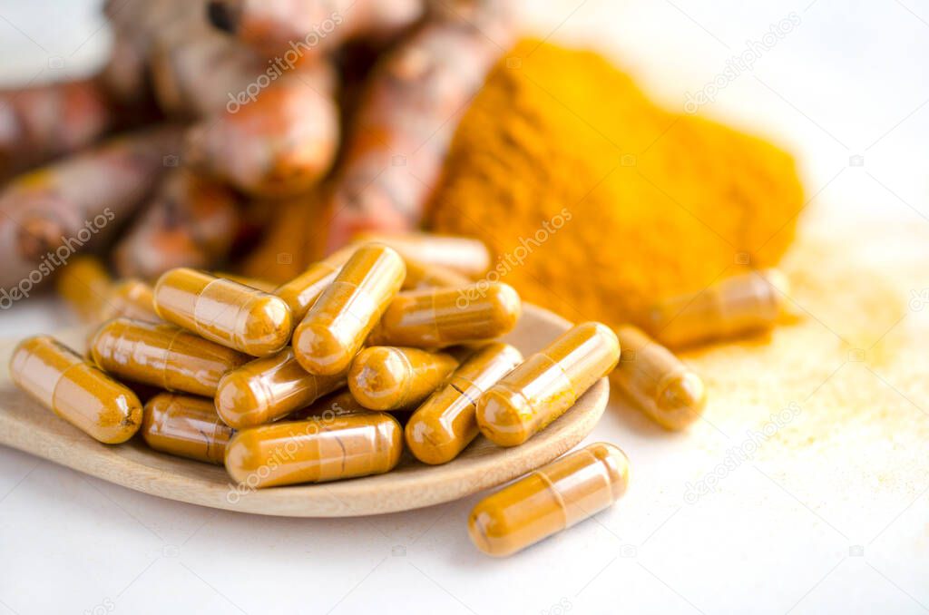 Closed up dry organic turmeric powder in capsule on wooden spoon on white background. For natural Thai herb medicine or alternative treatment product
