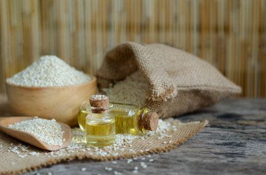 Kapalı susam yağı cam şişede, kuru çekirdekli çanta, tahta kase ve kaşık yumuşak sarı tonda.