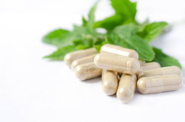 Kapsüldeki yeşil Tayland bitkisi tozunu beyaz arka plandaki bulanık yeşil bitki yaprağına yapıştırdım. Doğal ilaçlar ya da kimyasal alerjiden korunmak için alternatif tedavi seçenekleri