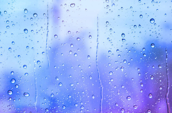 Abstract rain drop background on glass window panel over blur natural background in soft blue and purple tone