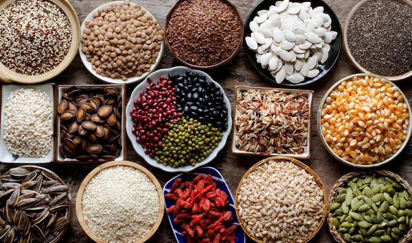 Collection of dry organic colorful cereal and grain seeds in wooden bowl in dark tone, consisted of bean, flax seed, goji berry, rice, peanut, job's tear, mung, and corn, for healthy food ingredient concept