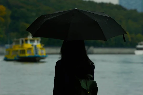 一个拿着黑色雨伞站在河边的女孩 — 图库照片