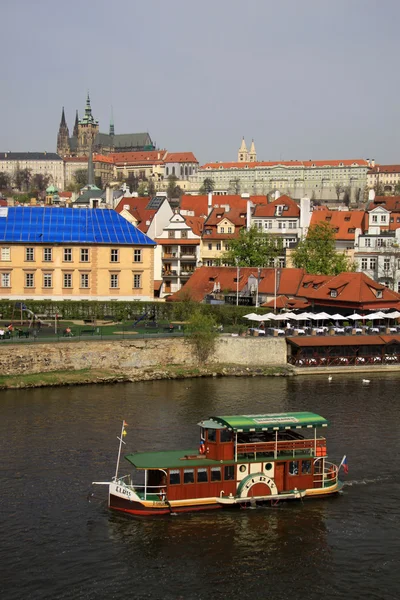 Prag, Tjeckien - 24 April, 2013: gammaldags båt flyter på floden Vltava längs Mala Strana bank och Pragborgen — Stockfoto