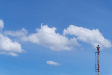 Endüstri kulesinin tepesinde kabarık beyaz bulutlar olan parlak mavi bir gökyüzü, temiz ve açık bir açık hava yaratıyor..