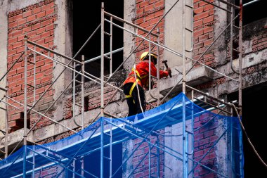 Güvenlik teçhizatı takan bir inşaat işçisi, inşaat alanında inşaat ve yapı onarımı üzerine çalışıyor..