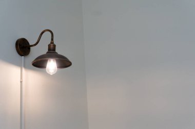 Ampullü lamba duvardan sarkıyor. Işık açık ve armatür metalden yapılmış.