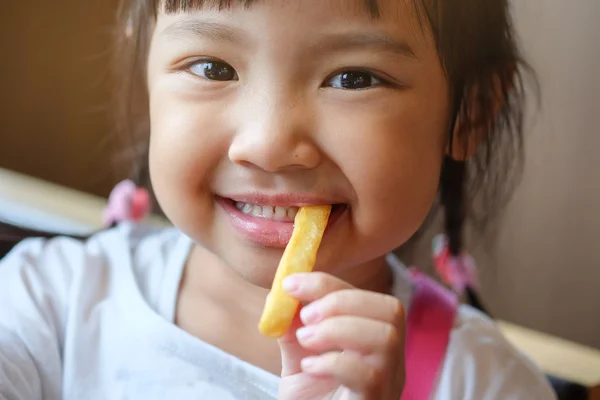 Χαριτωμένο ασιατικό κορίτσι χαρούμενος τρώει πατάτες τηγανιτές. — Φωτογραφία Αρχείου