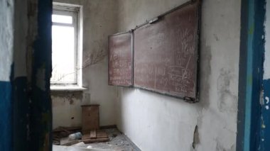 Terk edilmiş bir okul, sınıf, kırık camda karatahta, girişten manzara.