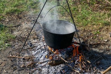 Şenlik ateşinde büyük bir kazan, alev, temiz havada yemek pişirme, izciler, orman açıklığı, dinlenme, yürüyüş, çocuk kampı, yaz, seyahat, turizm, tatil, yaz, yatay fotoğraf