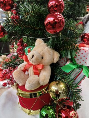 Boynunda kırmızı kurdele olan kahverengi ayı, kırmızı davulda oturuyor, yeşil dalların altında, yumuşak oyuncak, şirin, çok renkli katmanlar