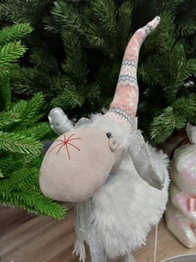 Beyaz koyun, yeşil sarmaşıkların altında duruyor, kırmızı kar taneli burun, gülümse, atkı, yüksek şapka, yumuşak oyuncak, şirin,