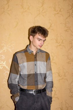 Turuncu duvarın yanında duran adam, profil, esmer genç, kahverengi gözlü, aşağı bakan, orijinal saç stili, elleri cebinde, ekose gömlek, siyah kot, öğrenci, genç adam, modaya uygun, model, poz veren, açık arkaplan