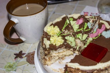 Kremalı dilimlenmiş çikolatalı kek, bir fincan kahve, masanın üzerinde tatlı, süslemeli, siyah krema, tereyağı çiçekleri, pastalar, jöle, lezzetli yiyecekler, havadar kremalar, beyaz hamurlar, kakao, mutfak, yatay fotoğraf, yakın çekim, üst görüş