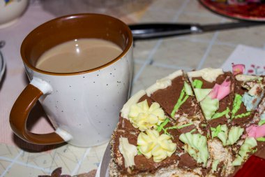 Kremalı dilimlenmiş çikolatalı kek, bir fincan kahve, masanın üzerinde tatlı, süslemeli, siyah krema, tereyağı çiçekleri, pastalar, jöle, lezzetli yiyecekler, havadar kremalar, beyaz hamurlar, kakao, mutfak, yatay fotoğraf, yakın çekim, üst görüş