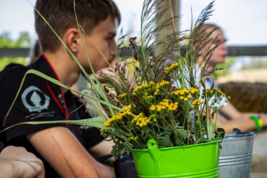 Masadaki koyu saçlı genç çocuk, bir buket kurumuş çiçek, sokak tahtası çardağı, sarı kızılötesi yüzükler, kır çiçekleri.,