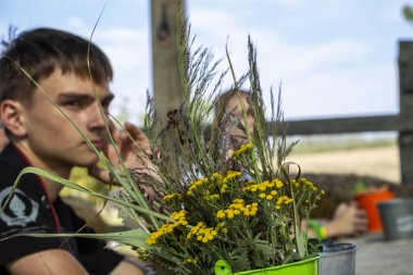 Masadaki koyu saçlı genç çocuk, bir buket kurumuş çiçek, sokak tahtası çardağı, sarı kızılötesi yüzükler, kır çiçekleri.,