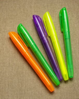 Metni vurgulamak için renk işaretleyiciler, turuncu, yeşil, mor, sarı, parlak floresan renkler, kapaklar, plastik, kırtasiye seti, kahverengi arkaplan, desenli yüzey, dikey fotoğraf,