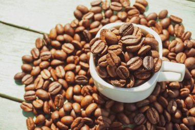 Kavrulmuş kahve çekirdekleri ve ahşap arka planda beyaz bardak..