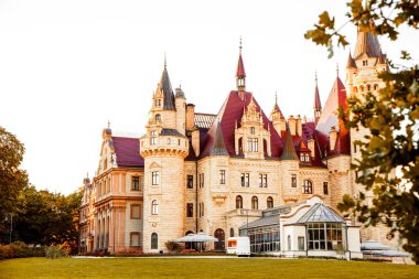 Realistic photo of a picturesque ancient fairy-tale castle on a green hill under a blue sky. Old stone fortress surrounded by nature and sunlight, evoking a magical medieval atmosphere. Perfect for travel, fantasy, architecture, and history themes.