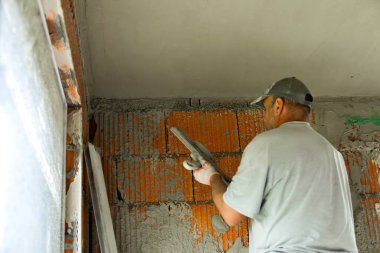 Tuğladan duvarları olan bir binanın iç tadilatı sırasında tavanı alçılayıp düzleştiren iki inşaat işçisi. Profesyonel müteahhitler sıva başvurusu ve duvar kaplaması üzerinde çalışıyor. İnşaat, onarım ve ev geliştirme kavramı.