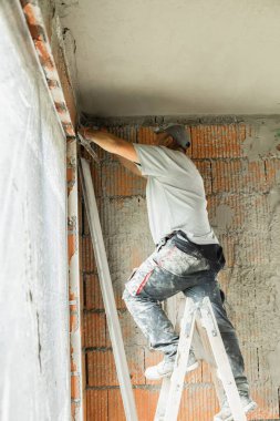 Tuğladan duvarları olan bir binanın iç tadilatı sırasında tavanı alçılayıp düzleştiren iki inşaat işçisi. Profesyonel müteahhitler sıva başvurusu ve duvar kaplaması üzerinde çalışıyor. İnşaat, onarım ve ev geliştirme kavramı.