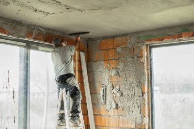 Tuğladan duvarları olan bir binanın iç tadilatı sırasında tavanı alçılayıp düzleştiren iki inşaat işçisi. Profesyonel müteahhitler sıva başvurusu ve duvar kaplaması üzerinde çalışıyor. İnşaat, onarım ve ev geliştirme kavramı.