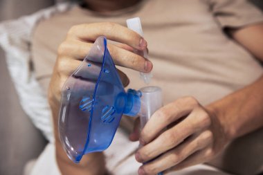 Evde genç bir çocuk nebulizör tutuyor ve solunum terapisinden önce onu ilaçla dolduruyor. Ev sağlığı, solunum hastalıkları, astım ya da soğuk algınlığı tedavisi kavramı. Solunum desteği için modern tıbbi cihaz.