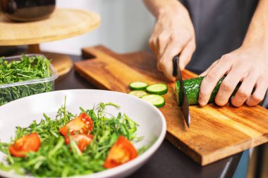 Mutfakta salatalık doğrayan mutlu genç çocuk taze sebze salatası hazırlıyor. Sağlıklı yaşam tarzı konsepti, otantik.
